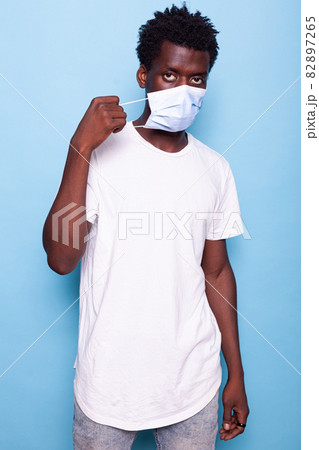 Portrait of person putting mask on face in studio Portrait of person putting mask on face in studio 82897265
