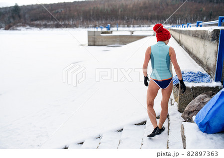Rear view of active senior woman in swimsuit getting ready for exercise outdoors in winter, cold therapy concept. 82897363