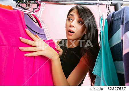 Beautiful young girl chooses clothes, outfit, dress in clothing store. Wow emotions, black friday, cyber monday, purchases, discount, ad. Beautiful young girl chooses clothes, outfit, dress in clothing store. Wow emotions, black friday, cyber monday, purchases, discount, ad. 82897637