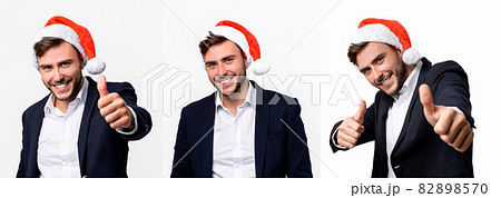 Young handsome caucasian guy in business suit and Santa hats stands on white background in studio smilie and showing thumbs up. Young handsome caucasian guy in business suit and Santa hats stands on white background in studio smilie and showing thumbs up. 82898570