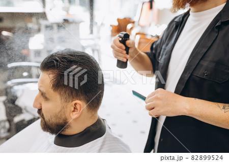 Man getting haircut at the barbershop. Professional barber at work process. Beauty, selfcare, style, fashion, healthcare and male cosmetics concept. 82899524
