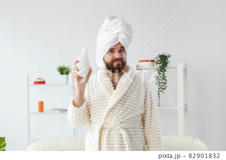 Beauty portrait of handsome beautiful guy in towel and bathrobe holding tube of body cream lotion in hand. Spa, body and skin care for man concept Beauty portrait of handsome beautiful guy in towel and bathrobe holding tube of body cream lotion in hand. Spa, body and skin care for man concept 82901832