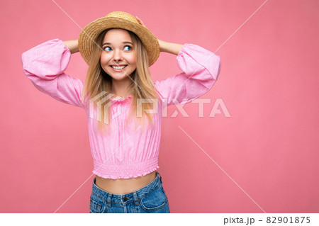 Portrait of young attractive smiling hipster blonde woman in stylish pink crop top and straw hat Portrait of young attractive smiling hipster blonde woman in stylish pink crop top and straw hat 82901875
