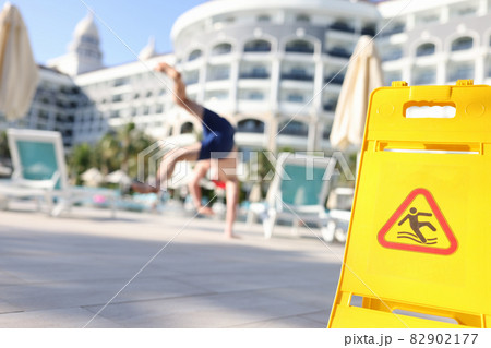 Young man falling on slippery tiles in street near yellow warning sign closeup 82902177
