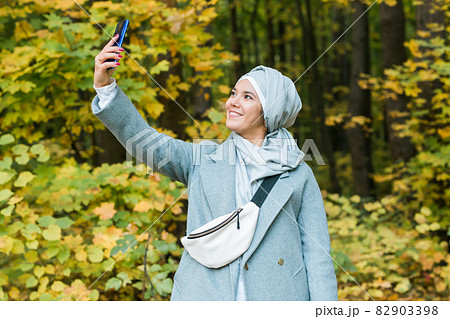 Young arabian muslim woman in hijab clothes doing selfie shot on mobile phone in park. People religious lifestyle concept. Copy space. Young arabian muslim woman in hijab clothes doing selfie shot on mobile phone in park. People religious lifestyle concept. Copy space. 82903398