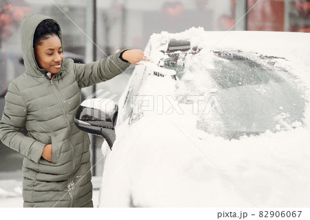 Woman removing snow from car windshield Woman removing snow from car windshield 82906067