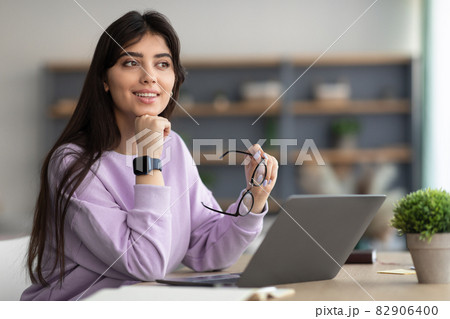 Pensive cheerful young female manager sitting at desk looking away 82906400
