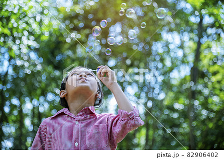 Adorable happy cute girl playful foam bubbles in green playground in summer outdoors. Funny Cheerful girl in the park with happy times. 82906402