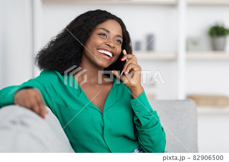 Happy african american woman sitting on couch, talking on phone Happy african american woman sitting on couch, talking on phone 82906500