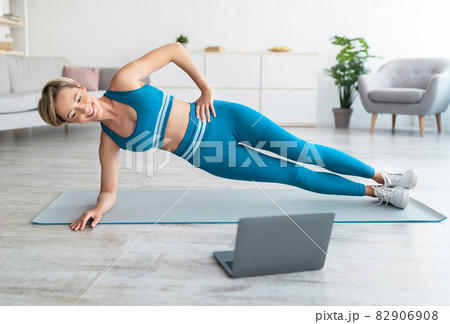 Smiling woman doing side plank on mat with pc Smiling woman doing side plank on mat with pc 82906908