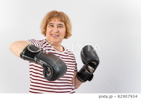 Elderly woman in fighting gloves in a defensive pose on a white background. Elderly woman in fighting gloves in a defensive pose on a white background. 82907934