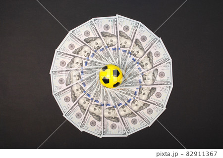 Football little ball lying on mandala kaleidoscope from money. Money and soccer ball - sport and business background. Football little ball lying on mandala kaleidoscope from money. Money and soccer ball - sport and business background. 82911367