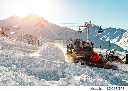 Red modern snowcat ratrack with snowplow snow grooming machine preparing ski slope piste hill at alpine skiing winter resort Ischgl in Austria. Heavy machinery mountain equipment track vehicle 82913563