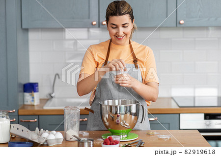 happy young woman cooking food on kitchen at home 82919618