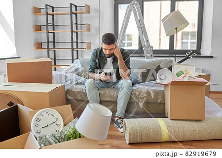 sad man with smartphone and boxes moving home sad man with smartphone and boxes moving home 82919679