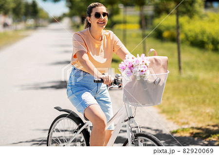 woman with flowers in bicycle basket in city 82920069