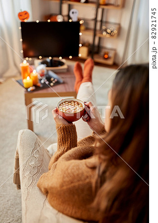 woman watches tv and drinks cocoa on halloween 82921745