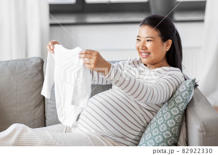 happy pregnant woman with baby's bodysuit at home 82922330