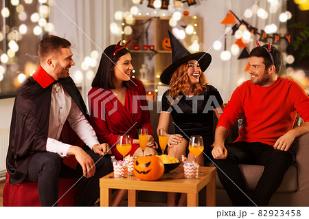 happy friends in halloween costumes at home party 82923458