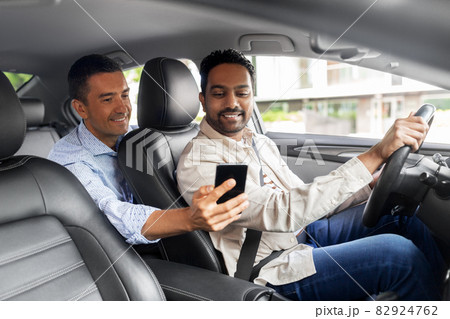 male passenger showing smartphone to car driver male passenger showing smartphone to car driver 82924762