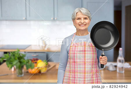 smiling senior woman in apron with frying pan 82924942