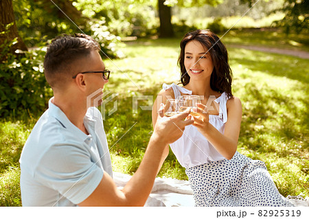 happy couple toasting drinks at summer park happy couple toasting drinks at summer park 82925319