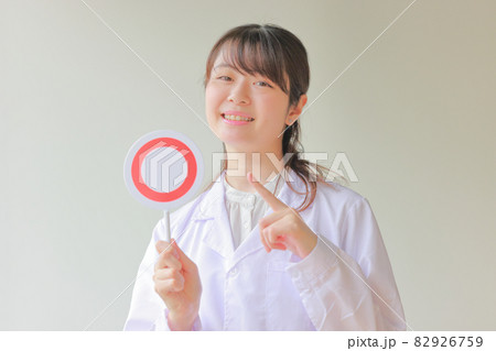 〇のプレートを持ち笑顔で指さす白衣女性1 82926759
