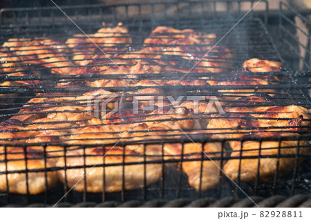 Chicken wings roasting on a grill on a charcoal grill. Smoke coming from the coals. Close-up. Selective focus. Backyard cooking concept Chicken wings roasting on a grill on a charcoal grill. Smoke coming from the coals. Close-up. Selective focus. Backyard cooking concept 82928811
