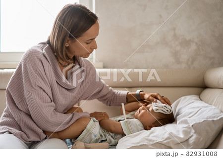 Young little boy on the sofa with cooler gel on her head and measuring temperature by thermometer 82931008