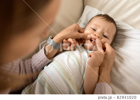 Cheerful cute baby boy lying on sofa while mother looking at his first teeth. 82931020
