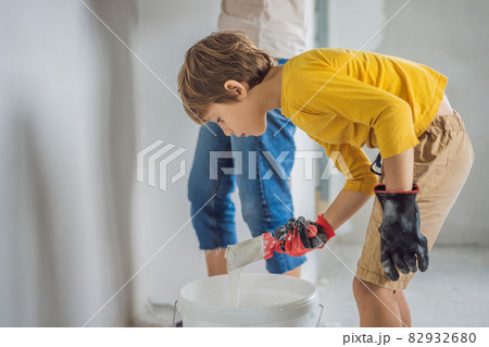 Woman with hir son makes repairs at home, she teaches boy to plaster the walls with a spatula in his hands Woman with hir son makes repairs at home, she teaches boy to plaster the walls with a spatula in his hands 82932680
