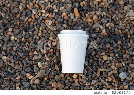 A white paper cup of coffee or tea lies on the rocky shore. A mug of hot drink on a pebble. Beautiful rocky background. free copy space. A white paper cup of coffee or tea lies on the rocky shore. A mug of hot drink on a pebble. Beautiful rocky background. free copy space. 82933176