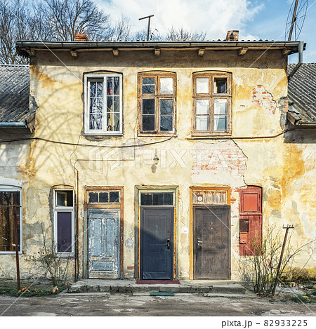 The facade of an old two-story house with different front doors and windows 82933225