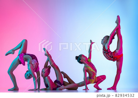 Group of beautiful flexible rhythmic gymnastics artists, girls in sport event isolated on gradient pink blue studio background in neon light 82934532