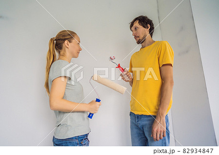 A man and a woman with rollers for painting the walls. A man with a very small bolster, symbolizing a small penis. renovation diy paint couple in new home painting wall A man and a woman with rollers for painting the walls. A man with a very small bolster, symbolizing a small penis. renovation diy paint couple in new home painting wall 82934847