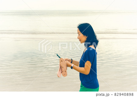 Woman walking on the beach looking at smart phone on vacation. 82940898
