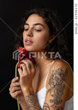 Cropped close-up portrait of beautiful tender woman with red gerberas posing isolated over dark background Cropped close-up portrait of beautiful tender woman with red gerberas posing isolated over dark background 82946170