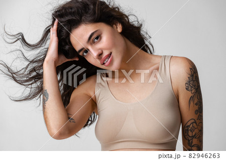 Cropped horizontal portrait of young woman with curly hair and nude makeup in beige inner wear isolated over gray background 82946263