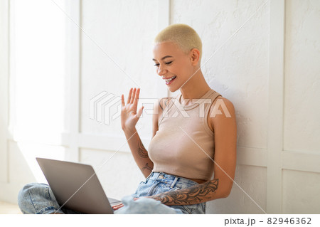 Online chat. Smiling caucasian lady making video call via laptop, waving hand to webcam, sitting over white wall 82946362