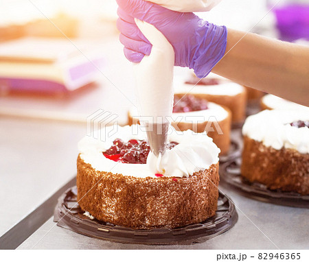 Pastry chef girl makes a cake from fresh biscuit berries and cream. Mass production of cakes and sweets, confectionery factory, professional 82946365
