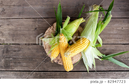 Natural cob of corn in husks on a wooden background. The concept of natural vegetables grown in their own garden, copy space for text Natural cob of corn in husks on a wooden background. The concept of natural vegetables grown in their own garden, copy space for text 82947723