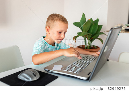 Little young school boy working at home with a laptop and class notes studying in a virtual class. 82949275