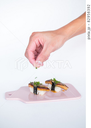 Japanese Sushi - Two Unagi Nigiri Sushi served on light pink board. Eel Sushi. Close-up view of process of preparing sushi. isolated on white 82956392