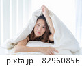 真っ白の布団から顔を出す寝起きの女性 82960856