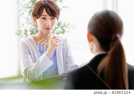 向かい合わせに座っているスーツを着た女性と会話するミドルの女性 82965324