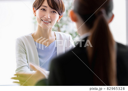向かい合わせに座っているスーツを着た女性と会話するミドルの女性 82965328