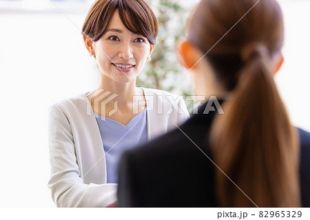 向かい合わせに座っているスーツを着た女性と会話するミドルの女性 82965329