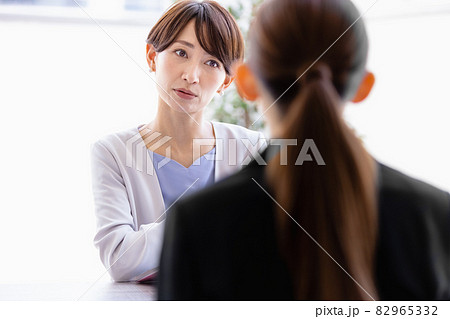 向かい合わせに座っているスーツを着た女性と会話するミドルの女性 82965332