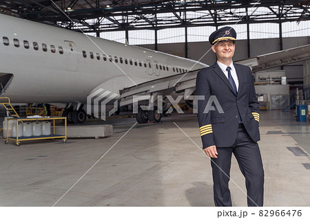 Smiling pilot posing against the backdrop of the aircraft in the hangar 82966476
