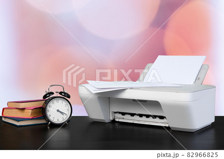 Compact home printer on desk with books against blurred background Compact home printer on desk with books against blurred background 82966825